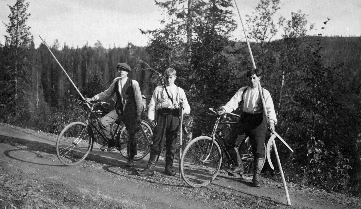 Tre unge menn fotografert i forbindelse med skogtaksasjon.  Mennene har skanter og klaver.  De to ytterste står med hver sin sykkel. Den midterste har et gevær over skuldra. 