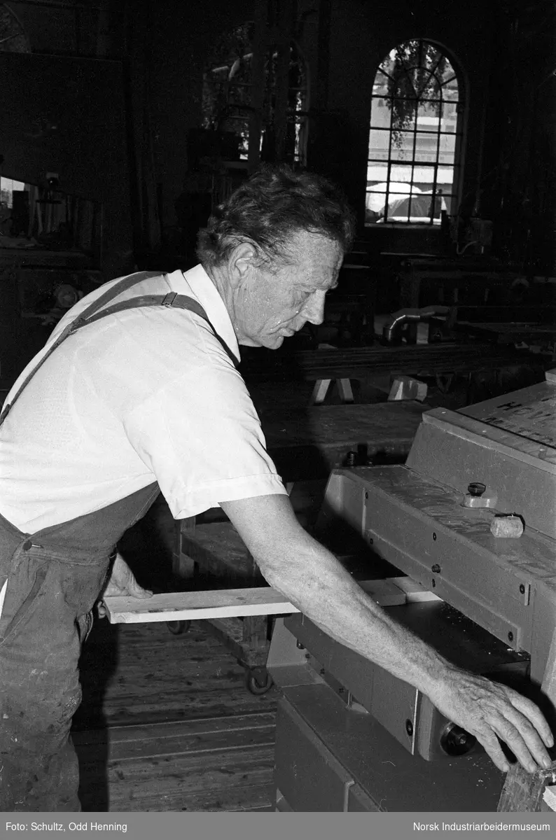Mann i arbeidsantrekk fra Norsk Hydro sager til planker på benk.