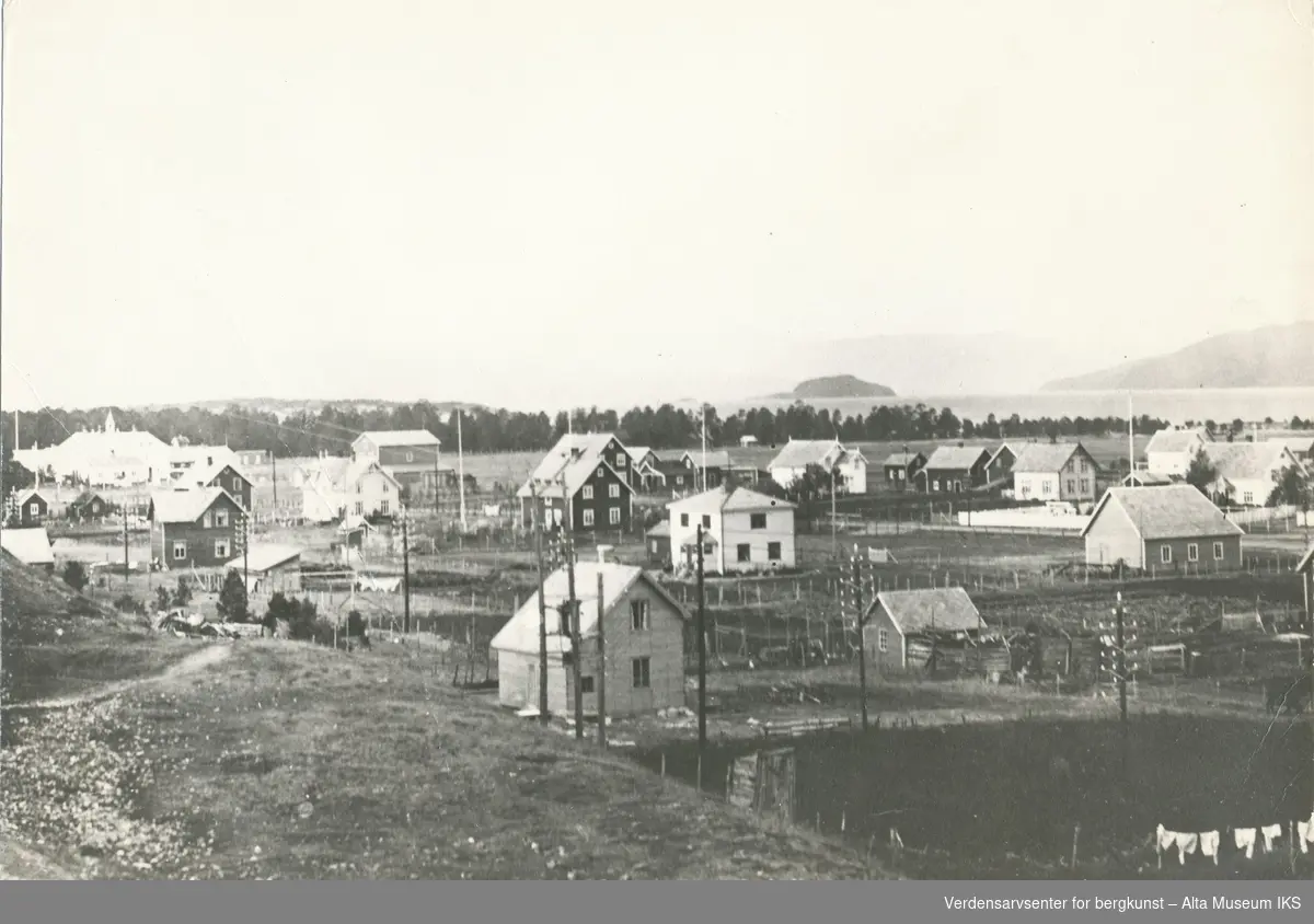Elvebakken, Alta. På bildet er det mange bygninger, både boliger og uthus. Helt til venstre er Altagård med Altagårdskogen og Amtmannsnes i bakgrunnen. Til høyre i bakgrunnen er Brattholmen og Altenesfjellet. Lengst ut i bakgrunnen skimtes Stjernøya.  

Foto E.Amundsen
