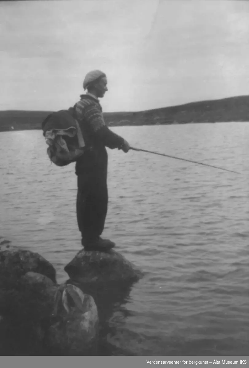 Mann med ryggsekk og fiskestang fisker ved et vann.