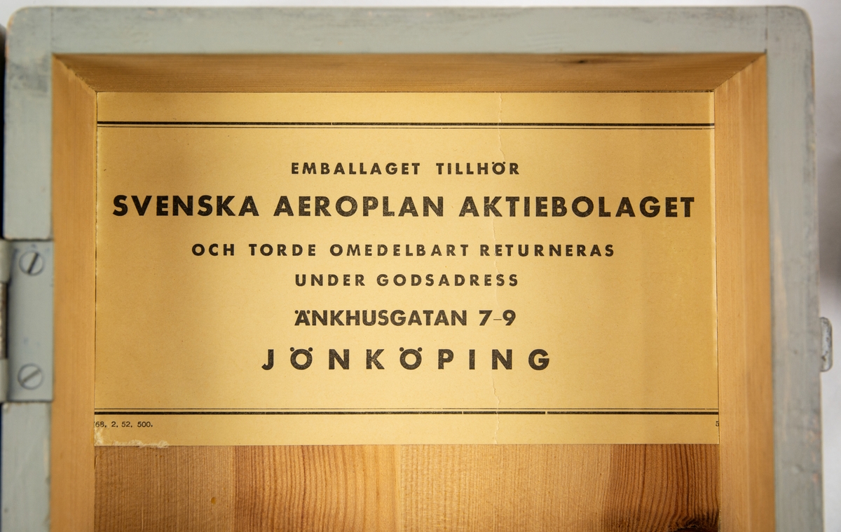 Fällmekanism BB3-1. Rektangulär box i metall. Förvaras i tillhörande transportlåda i trä. Emballaget tillhör Svenska Aeroplan Aktiebolaget Jönköping, låda nr 37.