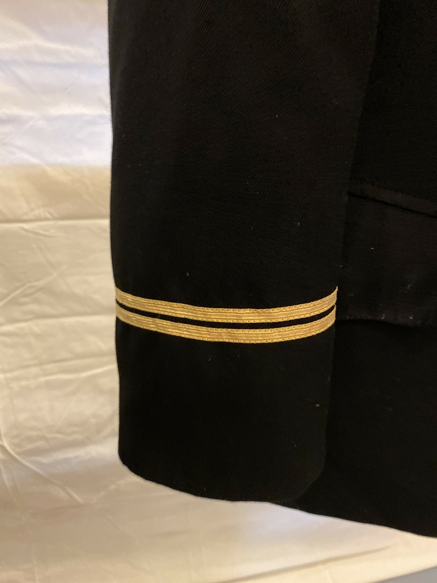 Uniformsjakke del av NSB-uniform, med lange ermer. Enkeltspent. Splitt bak. Gullknapper med Den norske løve. To brede gullstriper nederst på begge ermer. Gullstriper indikerer at bruker gjorde tjeneste på stasjonen, og to striper indikerte graden fullmektig.