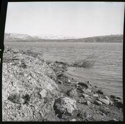 Fotografi av en fjære ved Lundfjorden med en sandbakke som d