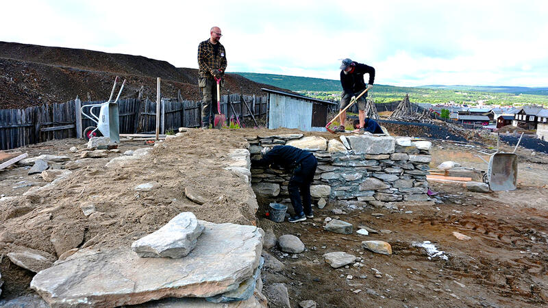 Bildet viser tre arbeidere som jobber med en mur. Muren er en kistemur. (Foto/Photo)