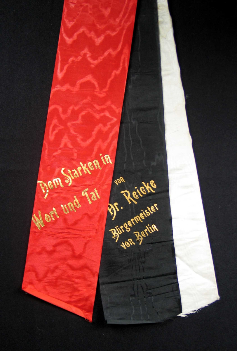 Begravelsessløyfe i rød, svart og hvit silke med tekst i gull.