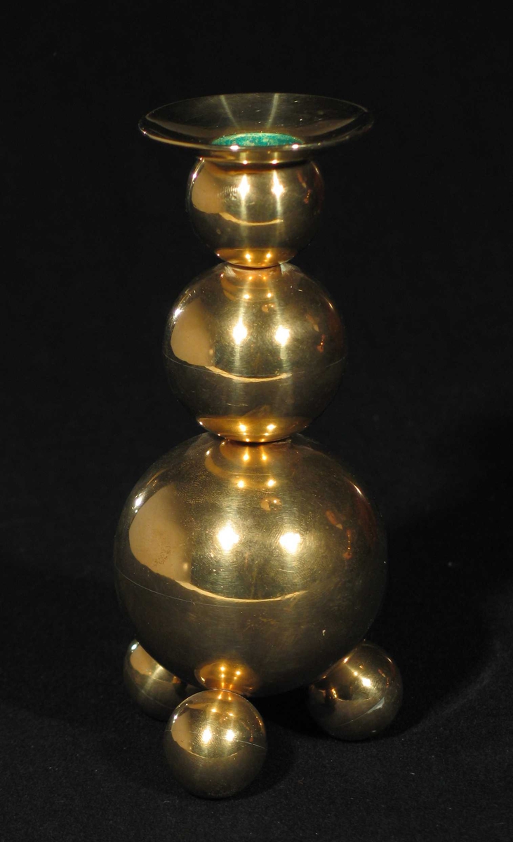 Lysestake i messing med tre runde fotknopper. Staken består av av stadig mindre kuler oppå hverandre. Fast mansjett.
