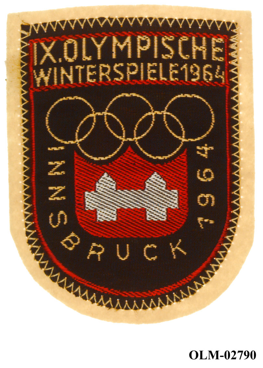 Skjoldformet jakkemerke med logo for de olympiske vinterleker i Innsbruck i 1964. I logoen er det motiv av de olympiske ringene og byvåpenet til Innsbruck.