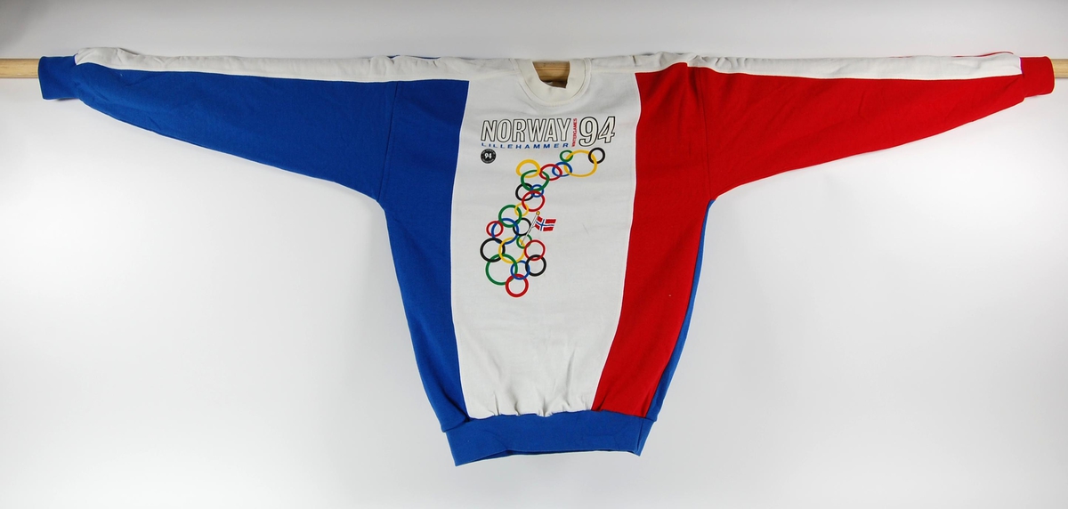 Flerfarget genser i størrelse medium med uoffisiell logo for de olympiske leker på Lillehammer i 1994. I logoen inngår de olympiske ringene formet som Norge.