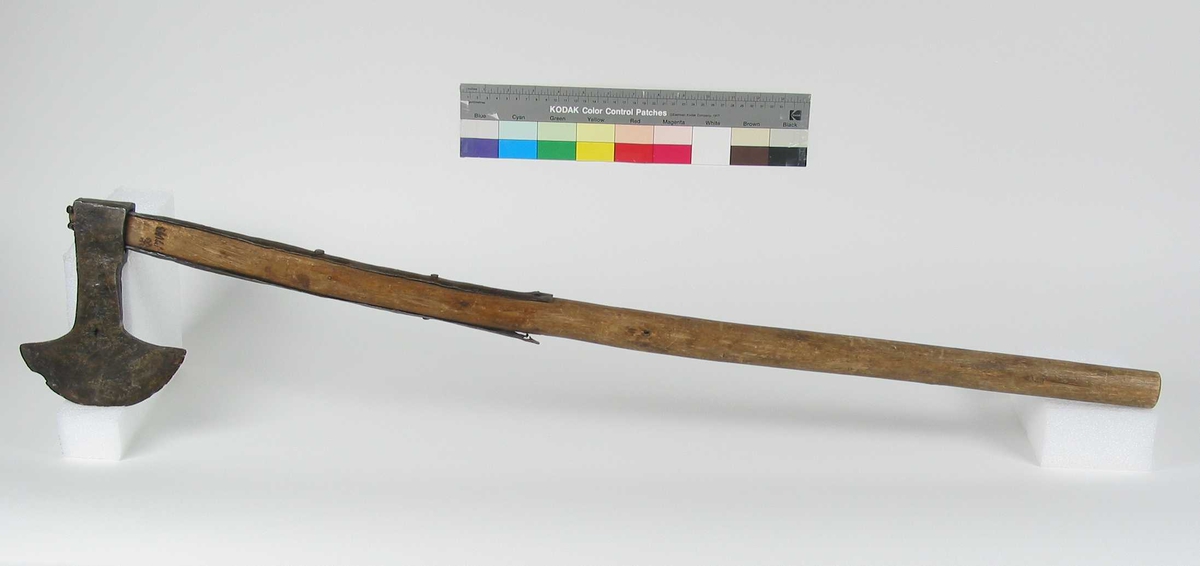 Symmetrisk økseblad.  Øksehammeren har skaftehull.
Over- og underliggende jernskinner som er ca. 41 cm. lange. 
Gammelt bruksskaft.