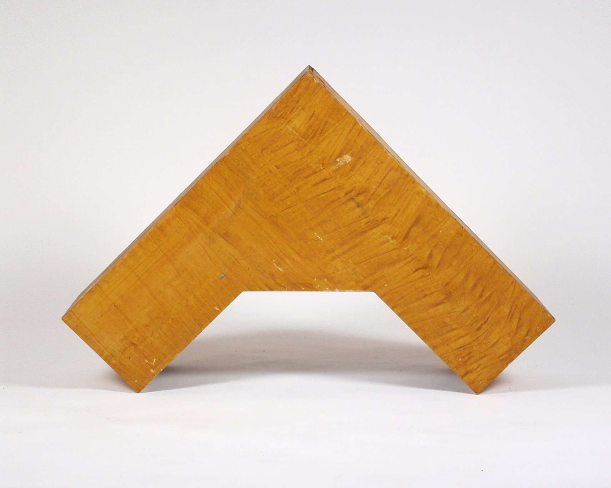 Bokhyllen er i malt tre og er trekant-formet, hjørnehylle.