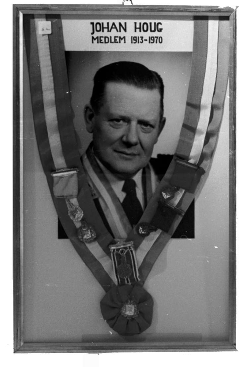 Portrett av Johan Houg. Rundt fotografiet henger ordensbånd i norske farger med fem medaljer.