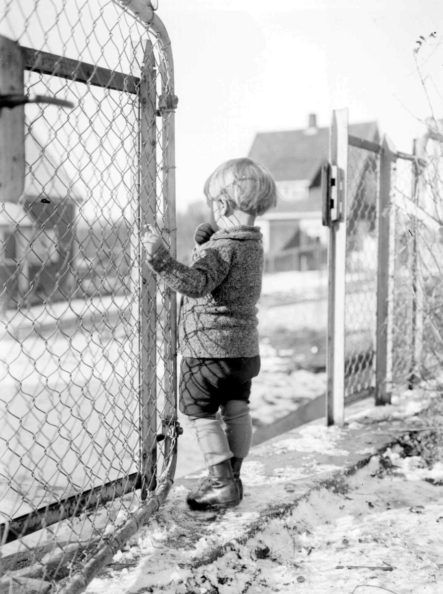 Vinter. Liten gutt i porten til lekeplassen. Gunnar Berge.
