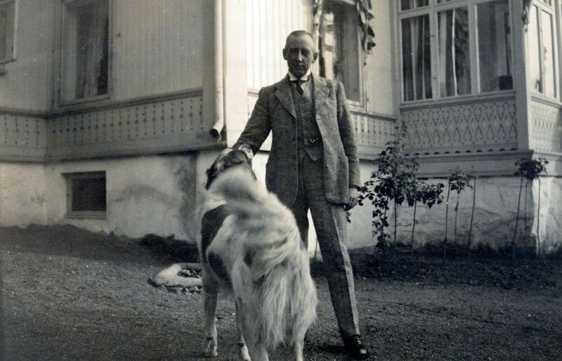 Mann står sammen med en hund foran hus.