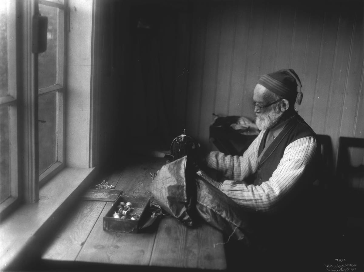 Landsskredderen i arbeid over symaskinen. Fotografert i juli 1907.
