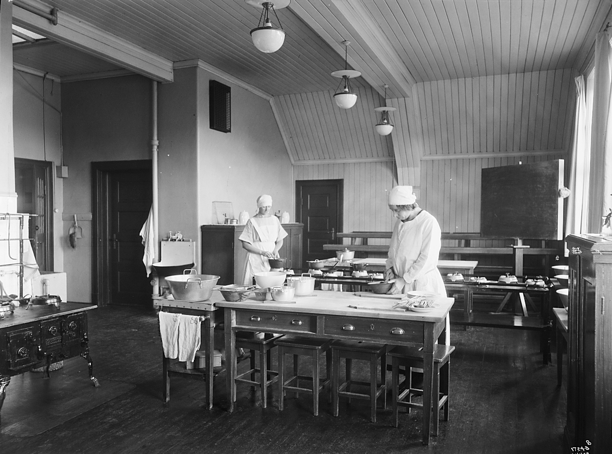 To kvinner fra Hjemmekonsulenten lager mat i et stort kjøkken på Ullevålsveien skole. Fotografert 1923.