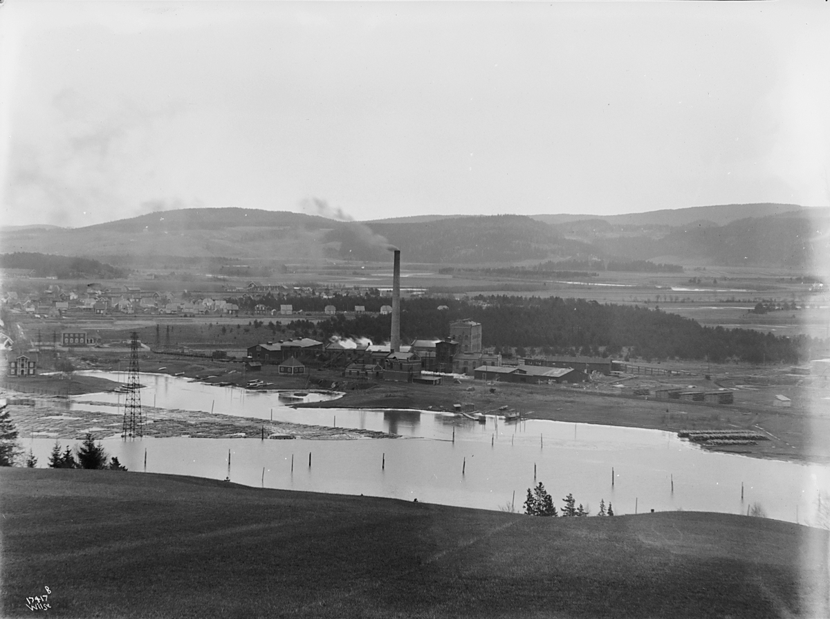 Fabrikkområde langs elv hvor det flyter tømmer, Lillestrøm cellulosefabrikk. Fotografert 1923.
