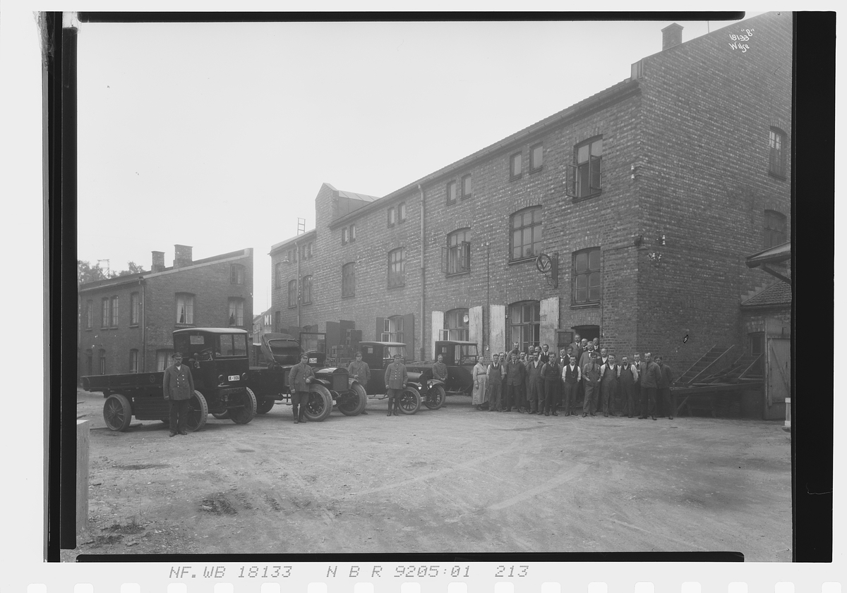 Ansatte, sjåfører og biler står utenfor bygning til Vinmonopolet. Fotografert 1924.