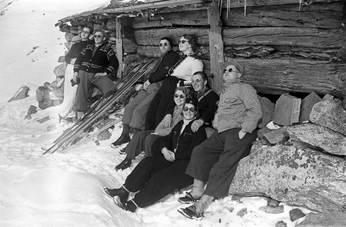 Åtte påsketurister soler seg ved seterbygning i fjellheimen. Fotografert 1940.