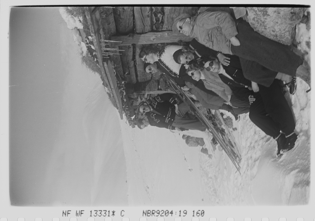 Åtte påsketurister soler seg ved seterbygning i fjellheimen. Fotografert 1940.
