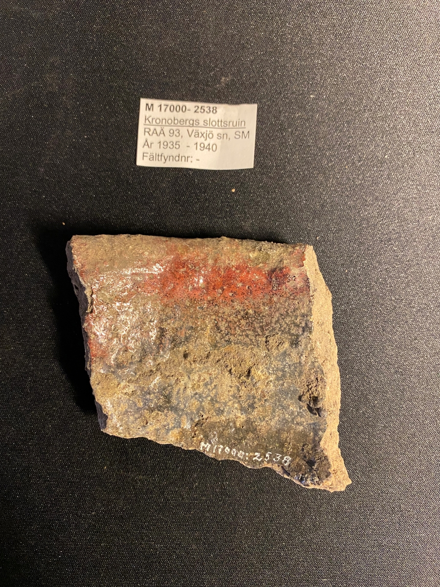 Fragment av mynningsbit till en degel. Sekundärt bränd med delvis cintrade röda till gröna ytor på in- och utsidan. Relativt grovt gods. Sammanhör med M  17000-2539.