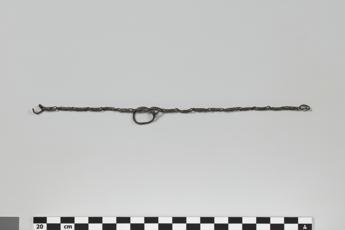 Stolpeband (mål for kyr), lenke av bronse med 17 ledd (spiralopprullinger), lengde 19,8 cm (H1006/II).