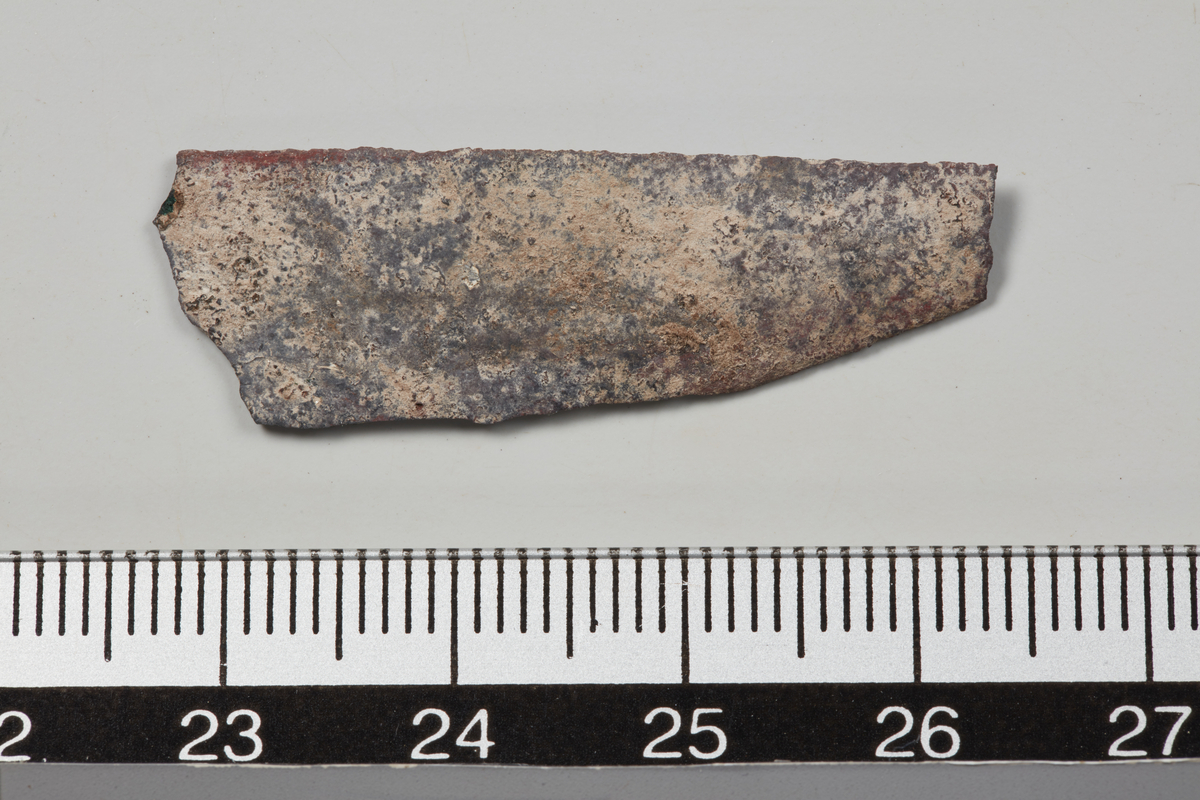 Fragment av knivblad av jern, tynt. Mulig barberkniv. Lengde 5,7 cm, største bredde 1,2 cm.