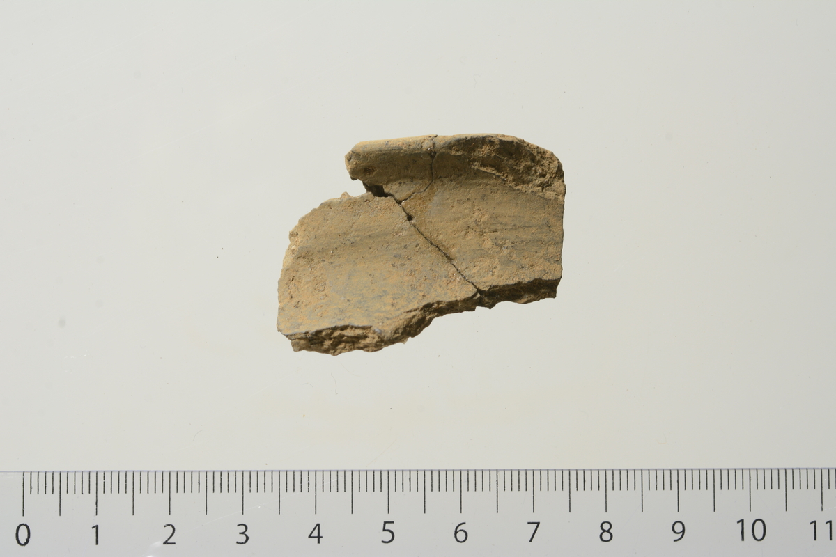Fem fragmenter (rand, hals) av et tynt leirkar av sortglittet gods som sammenlimt danner en del av munningsrand til et kar.