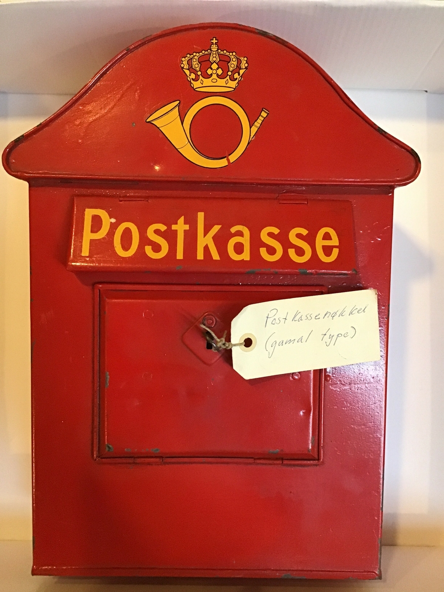 Raud postkasse, med postens logo, for levering av brevpost. Raude postkassar var låst, her ser me nøkkelen står i, og  dei vart regelmessig tømde av postbudet.