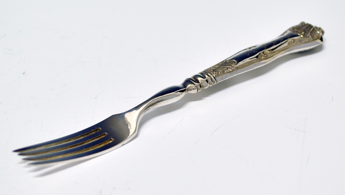 Gaffel med skaft. Tilhører antakeligvis bestikksett med skje og kniv. Gaffel med fire tinder satt tett sammen. Skaftet har muslingmønster i relieff. Det er inngravert C.C.C.A. 1835.(Christine Cecilie Carlotte Aall) på skaftet.