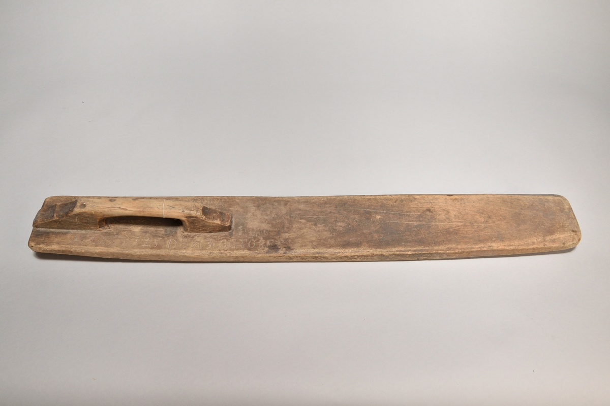 Kaveldon tillverkat i trä, med platt bräde samt handtag. Ovansidan med inskriften: "ANAO 1725 DEN 3 OCTOBER". 