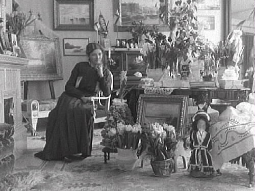 Hulda Lindh firar sin 50-års dag i salongen i "Rancheborg", 1916-02-11. Hulda är syster till fotografen, Mathilda Ranch, och sitter vid kakelugnen omgiven av blomster och presenter.