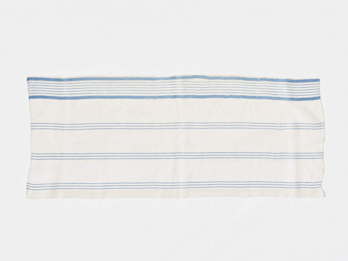 Kappegardin til to vinduer, a og b:
Tøyet er toskaftsvevd. Hvit bunn har 8x8 tr/cm. Blå striper langt tettere. Stripene ligger i renningen. 12 cm bred bord i ytterkant av fem smale små striper innenfor 1,7 cm brede blå striper. Ut over flaten er det fordelt tre stripeenheter med tre, smale blå striper i hver, totalt med hvit botn måler hver enhet 3 cm. Stripene får effekt av renningsrips.
Søm: Tøylengden er brukt på tvers av vinduet. Stripene går derfor på langs av gardinkappa. Bred, blå bord nederst på kappa, der det er en ca 3 cm bred fald. Ellers smale falder i hver side. Øverst er jaren brukt i 4 cm fald som er løpegang for opphenging.
Gardinene er noe stivet. 