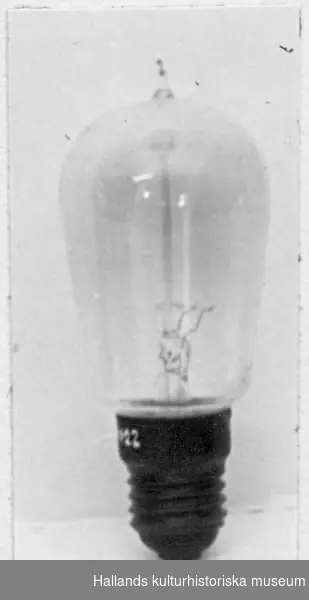 Glödlampa, päronformad, upptill avslutad i en spets. Handblåst av klart glas med gängad metallsockel (Edisonsockel). Mitt i lampan en glasstång och metalltrådar (glödtråd, av volfram?). Längd: 12,5 cm.