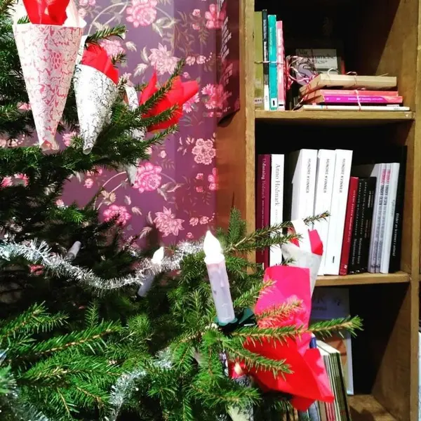 Nærbilde av juletre i museumsbutikken. I bakgrunnen ser man den ene bokhyllen og det lilla blomstertapetet. Juletreet er pyntet med glittergirlander, juletrelys og kremmerhus.