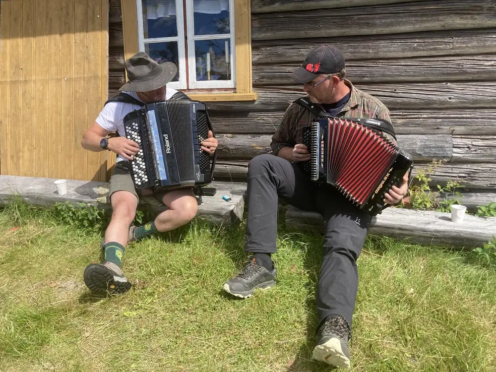 To menn spiller trekkspill ved en tømmervegg på Skålbergsætra.