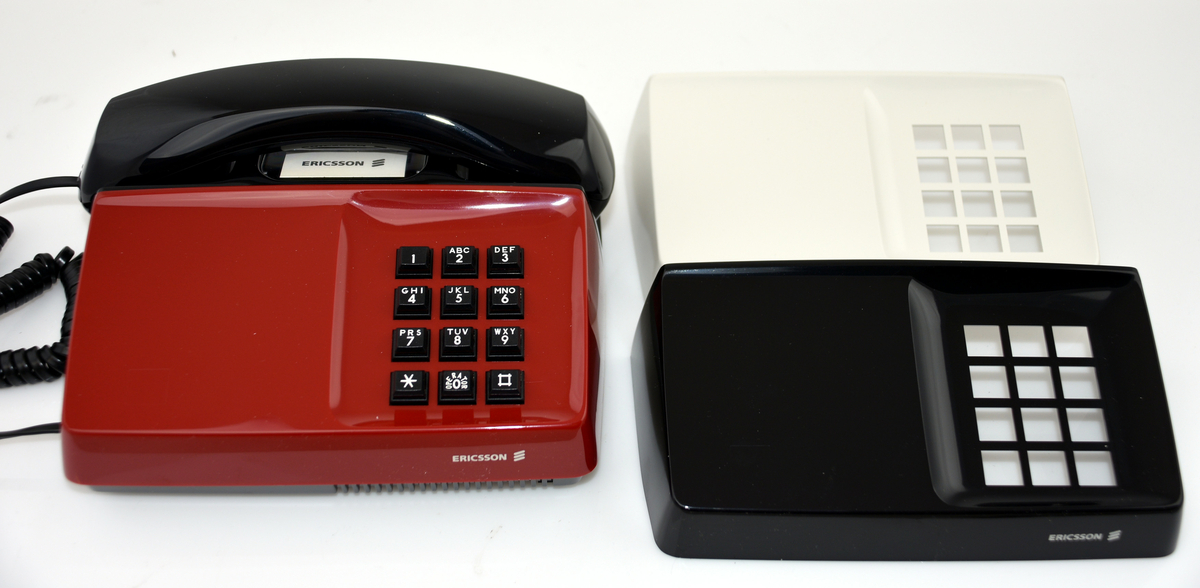 Telefonapparat, Diavox 'The Ericsson Royal 100', för export till USA, år 1984. För AT-system, huvudapparat, anknytningsapparat till abonnentväxel och sidoapparat. Bordsmodell med kåpa och mikrotelefon av svart plast, knappsats med 12 knappar för tonval, högohmig reglerbar ringklocka, elektretmikrofon och elektronisk talkrets med automatisk dämpningskompensering. I originalkartong med två extra apparathöljen i rött och vitt.