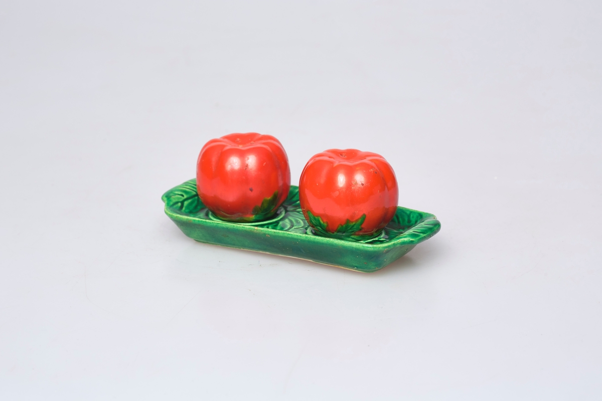 Salt- og pepperbøsse har motiv og farge som en tomat. Fatet (a) er grønt og har motiv av blad.