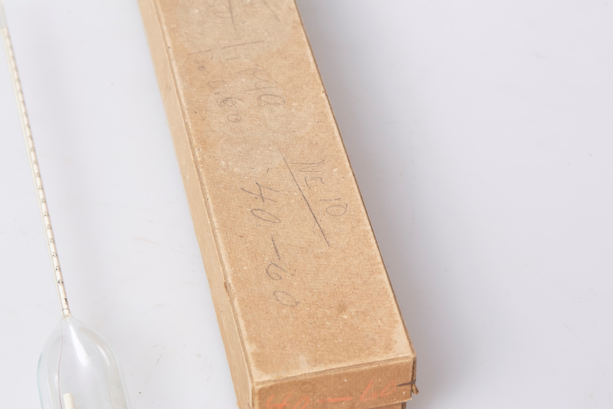 Lactodensimeter (a) oppbevart i en tilpasset eske av papp (b og c). Inne i røret ligger en lapp med følgende påskrift: "Lactodensimeter Temp 15 C oben ablesen". 