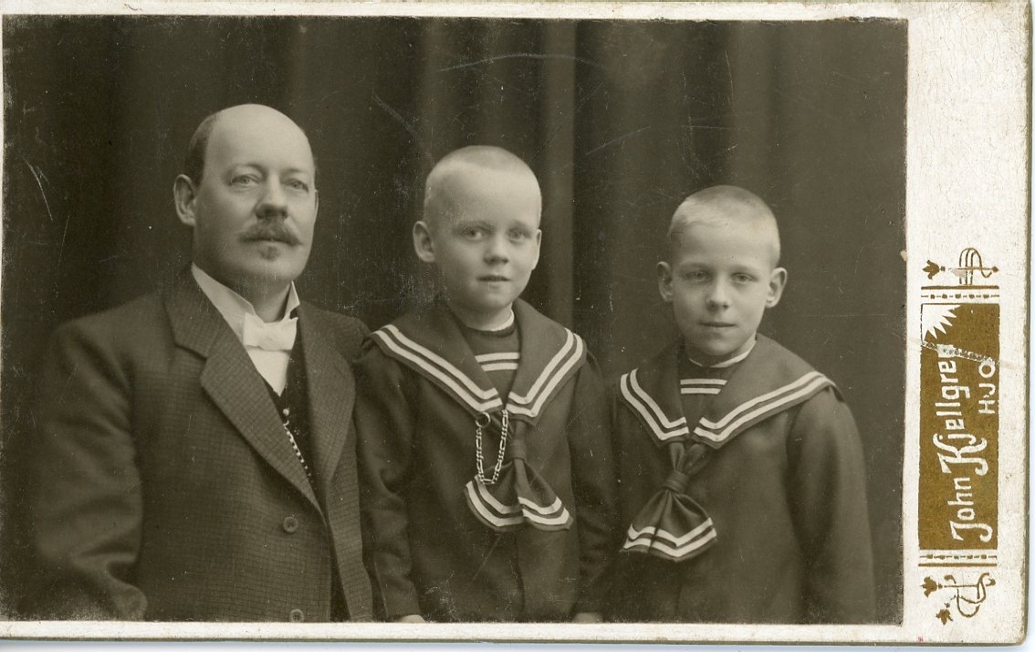 Kabinettsfotografi av en okänd man med klockkedja. Intill honom står två pojkar i sjömanskläder.