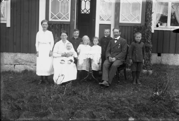 Familjebild i trädgården framför bostadens veranda, makarna och deras sju barn.