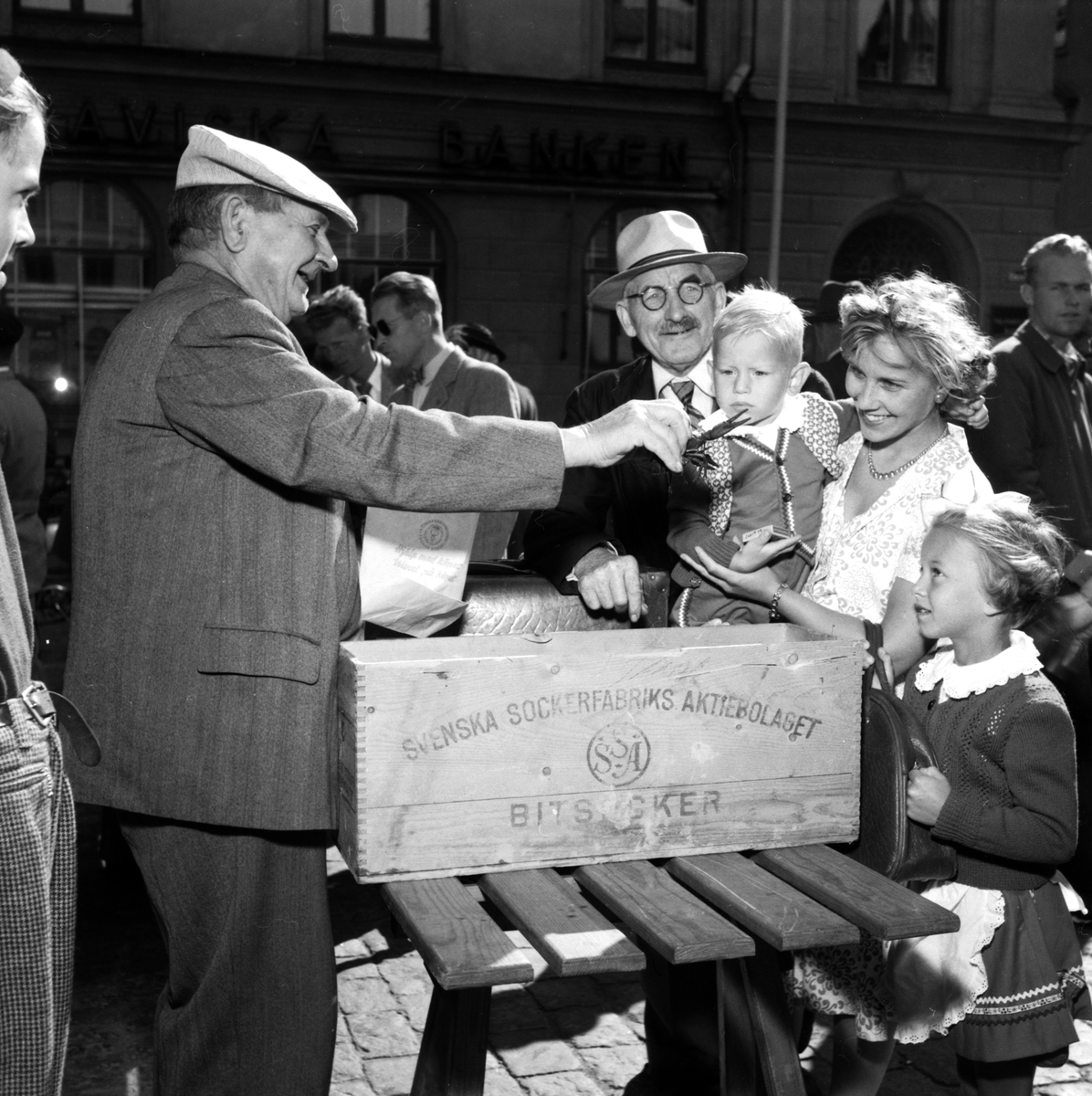 Karl Oskar "Kalle-Nisse" Nilsson får små som stora kunder att fascineras av storkloade kräftor. Ögonblick från 1953 års kräftförsäljningspremiär på Stora torget i Linköping.