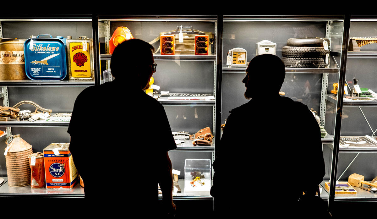 Silhuett av to besøkende foran et glassmonter med gjenstander på utstillingen Drift