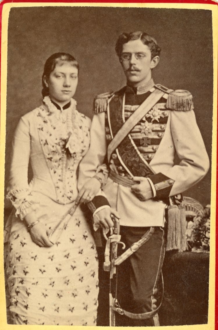 Kabinettsfotografi av en ung kvinna och man, den senare i militär uniform med höger hand på en värja.
