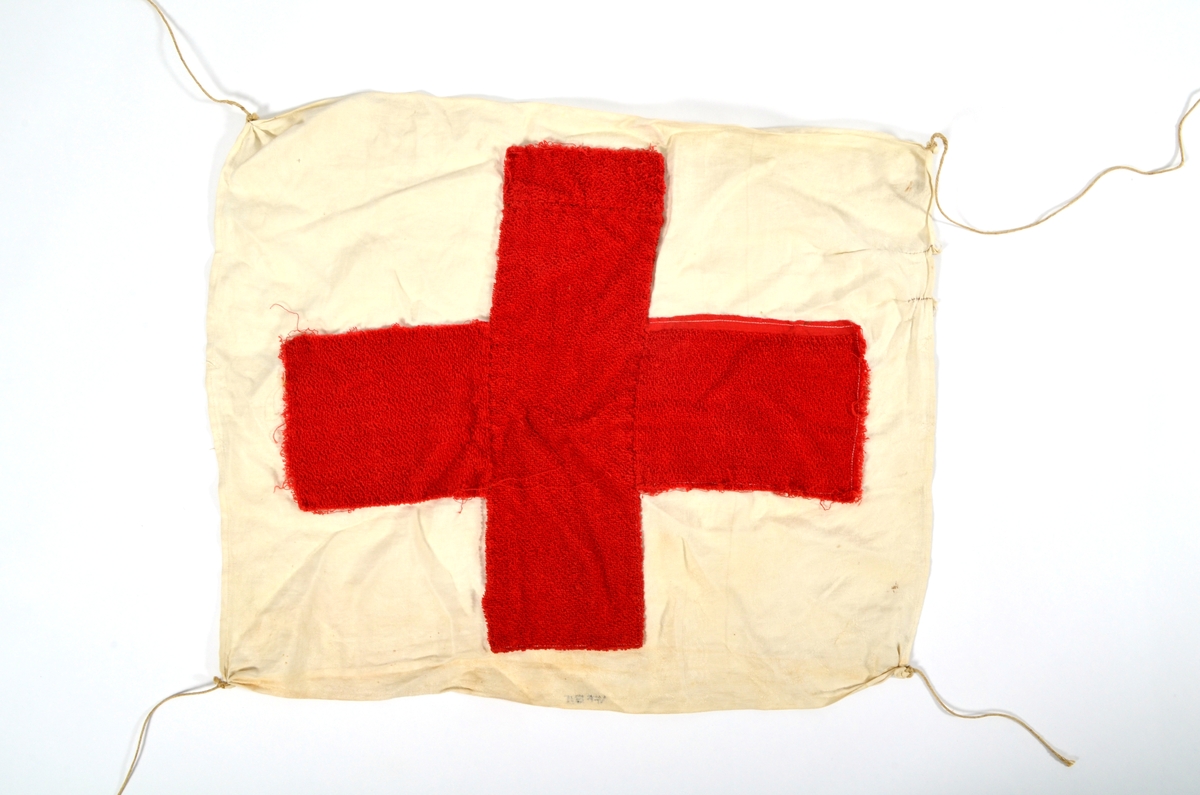 Røde kors flagg laga av eit kvit mønstervove tøystykke (sannsynlegvis eit kjøkkenhandkle), påsydd ein kors i raudt frotté tøy.