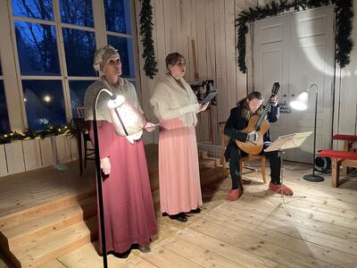 Mona Julsrud og Ingrid Grimdalen synger i Rikssalen akkompagnert av gitarist. Damene er ikledd kostymer ala 1814.
