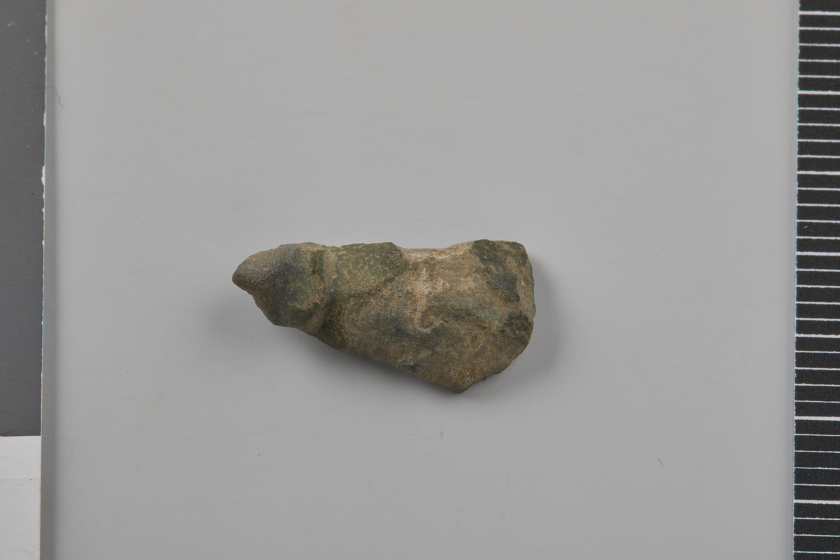 Fragment av bøyle til likearmet spenne av kobberlegering, fra folkevandrings- eller merovingertid. En liten bit av nålholderen gjenstår på baksiden. Nåværende l. 1,7 cm, b. 0,9 cm, t. 0,2 cm. Vekt: 1,4 g.