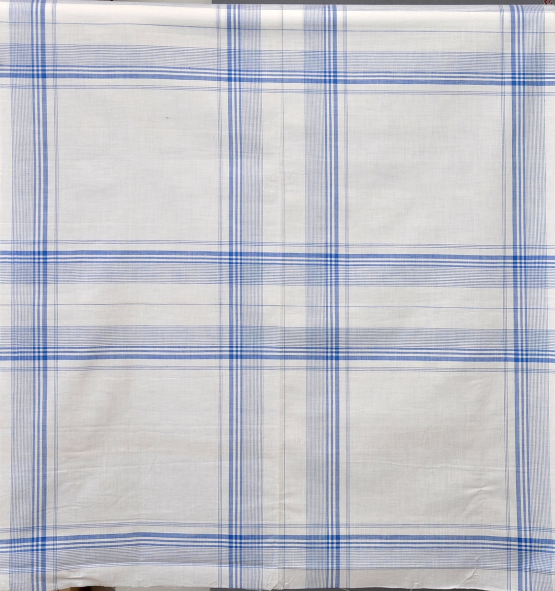 Näsdukar i bomull, 1940-tal.
Vävt mönster med blå bård och bottenrutning på vit botten.
Otvinnat garn.
Vävda 2 i bredd med en markering i klipplinjen.
51,5 x 53,5 cm.