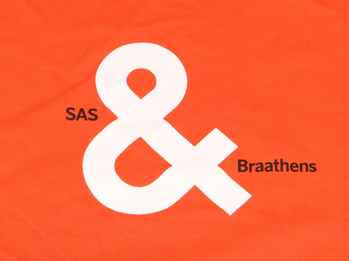 Oransje t-skjorte med rund hals. Liten SAS Braathens-logo på brystet, og større motiv på ryggen. Størrelse L.