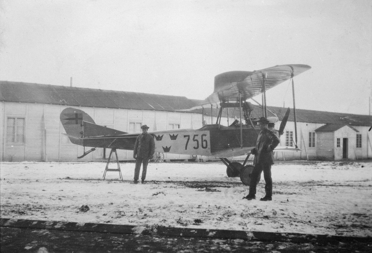 Flygplan Albatros NAB 9 nummer 756 tillhörande Flygkompaniet står uppställd på bock på flygverkstäderna Malmslätt, vintertid omkring 1917-1924. Två militärer vid flygplanet.