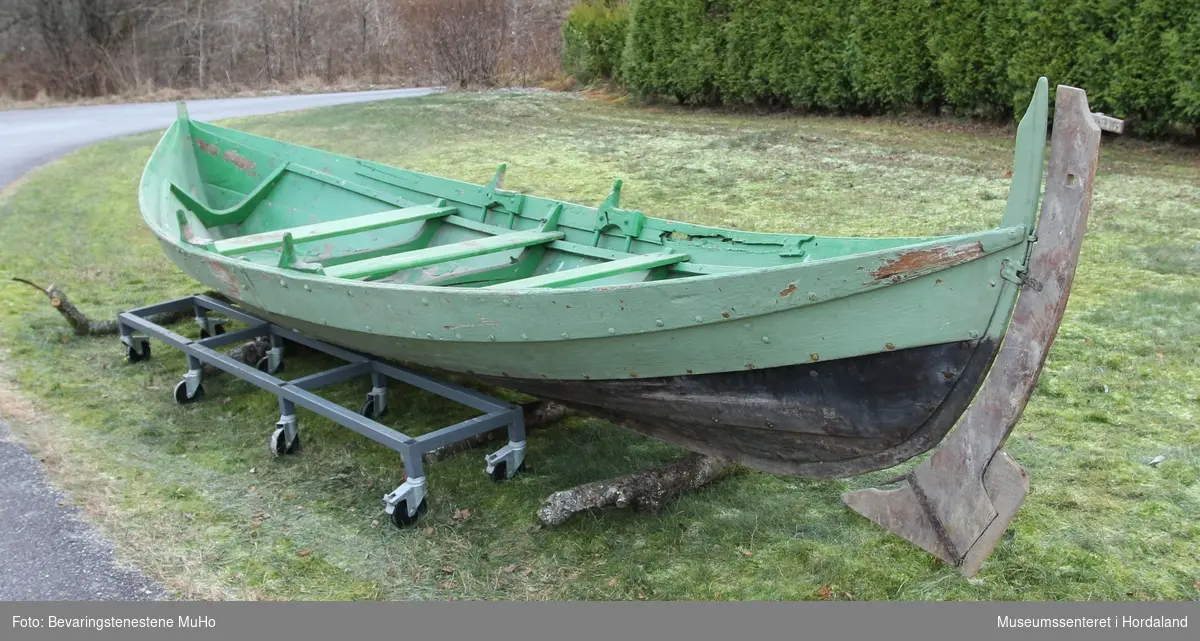 Båt av lokal båttype antageligvis fra Osterfjorden, klinkbygget, med fire bord og fire keiper. I tillegg består den av tilfar: et ror og en nygle, tre tofter og fem tiljer. Øvre del av båten er grønnmalt, mens bunnen er svartbeiset.